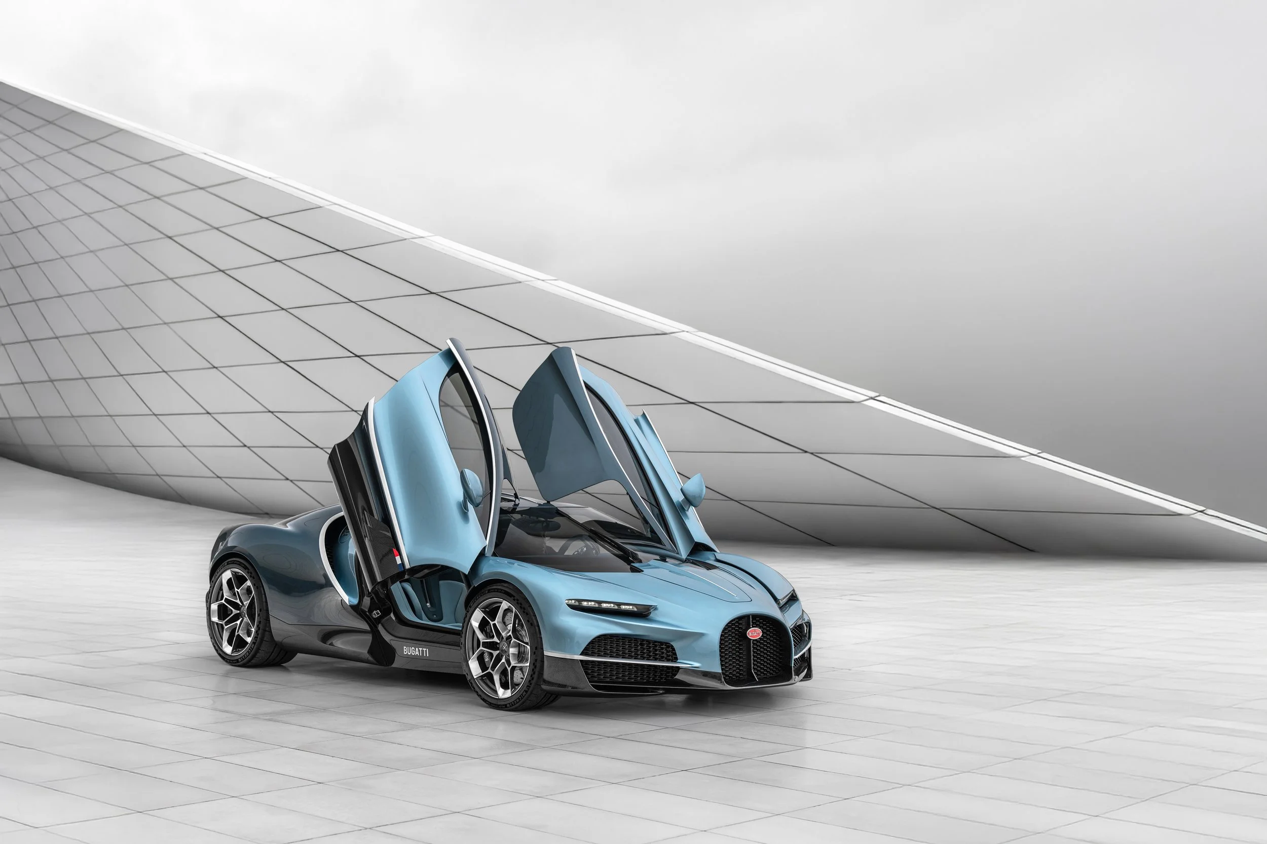 A sleek blue Bugatti sports car with butterfly doors open, parked on a light-colored tiled surface in front of a modern, curved metallic building.
