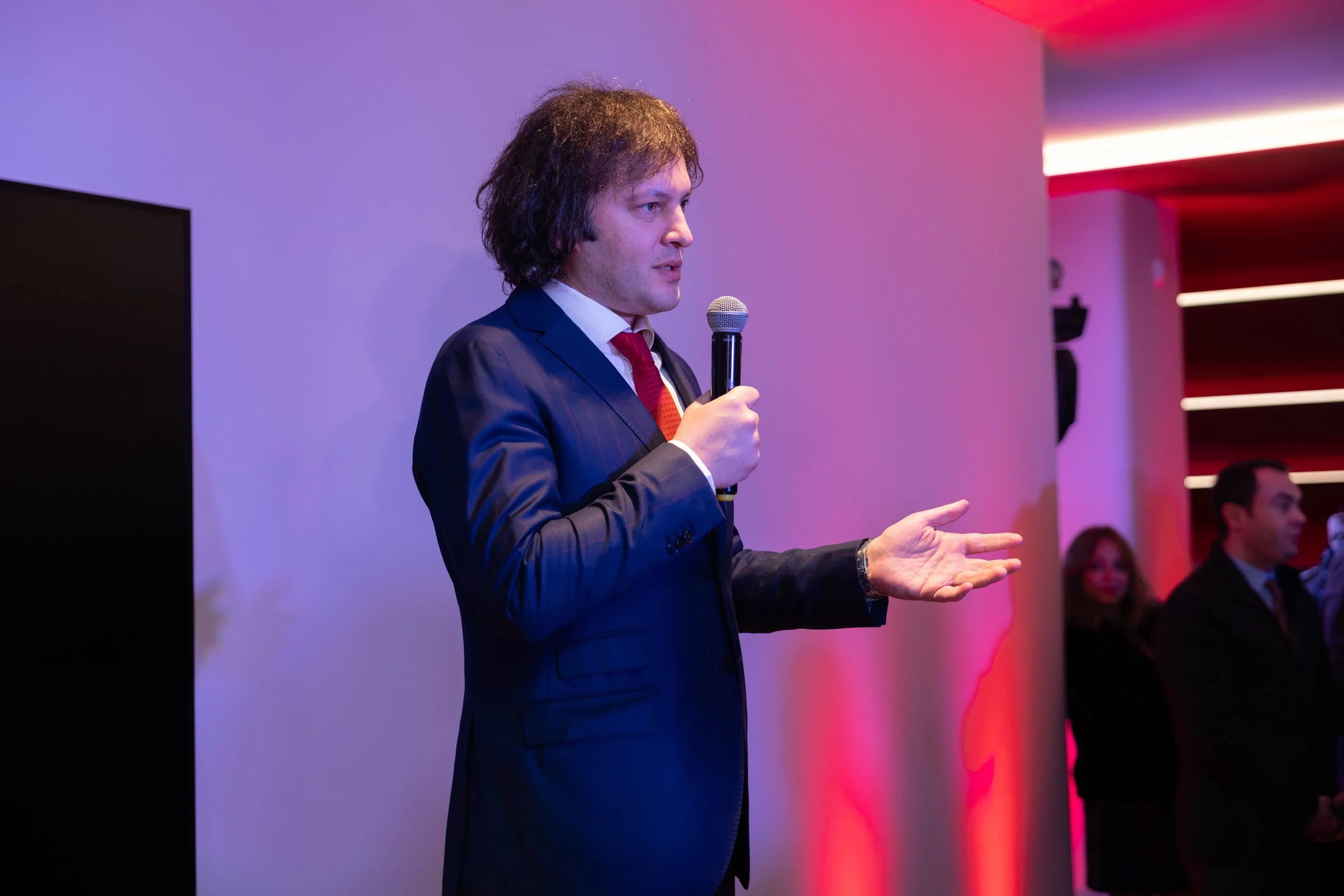 A sleek, modern sports car parked at night in front of a futuristic building with large glass windows and an undulating roof.