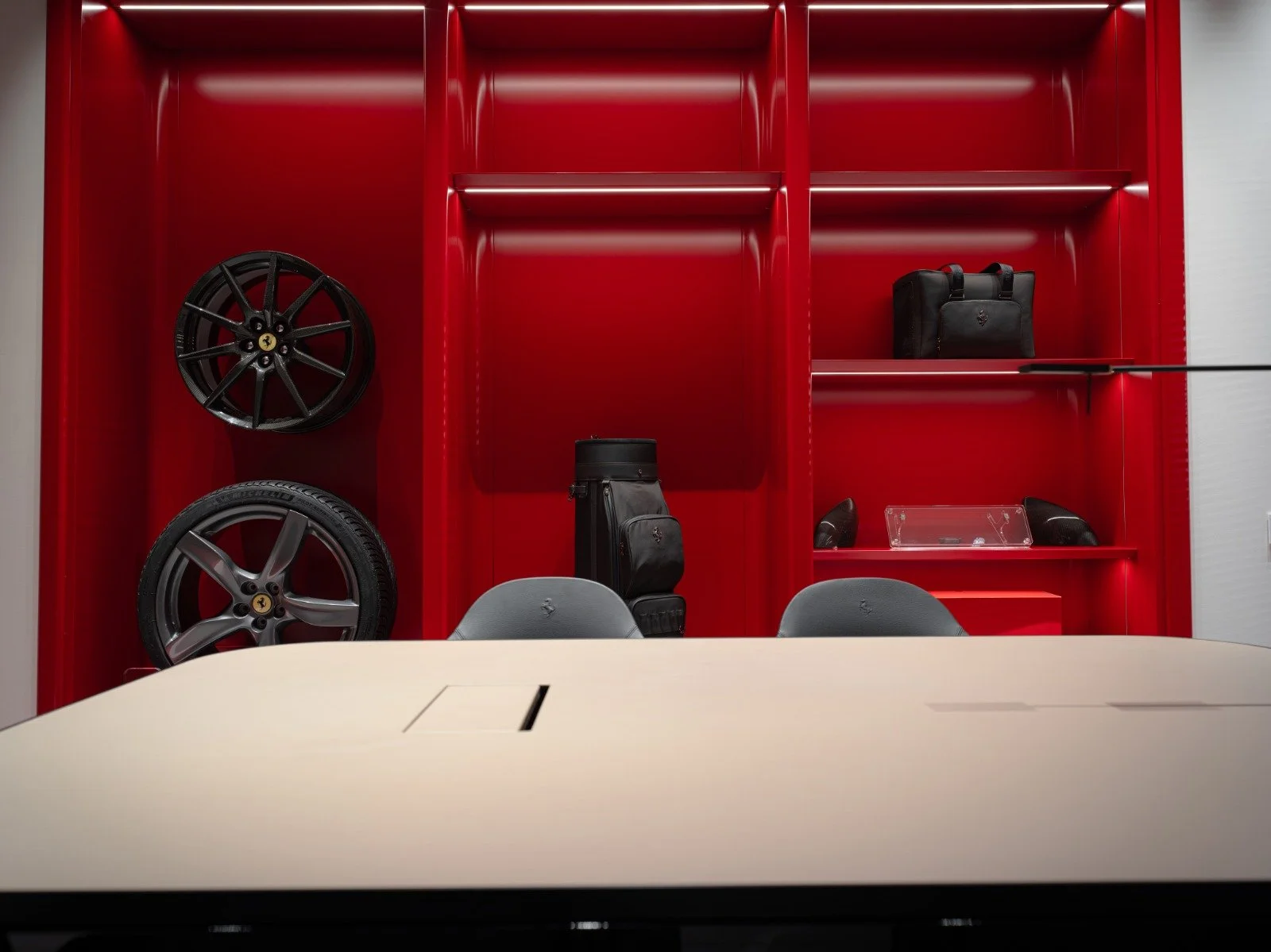 Red shelving unit with black car wheels, a black bag, and a black briefcase, seen from behind a conference table and chairs.