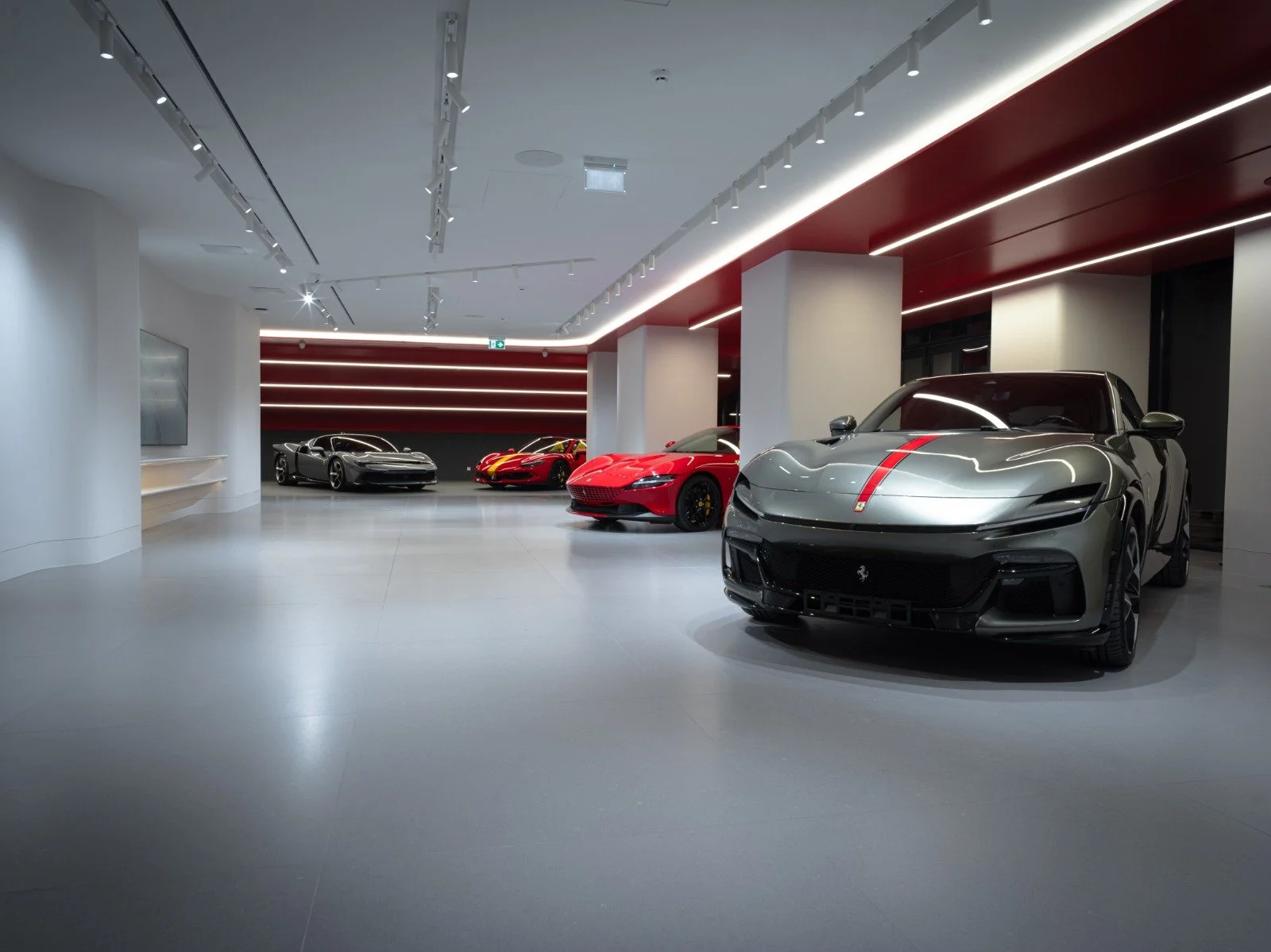 Luxury car showroom with five high-end cars, including Ferrari and Porsche, displayed on a sleek, modern interior with white and dark red accents.