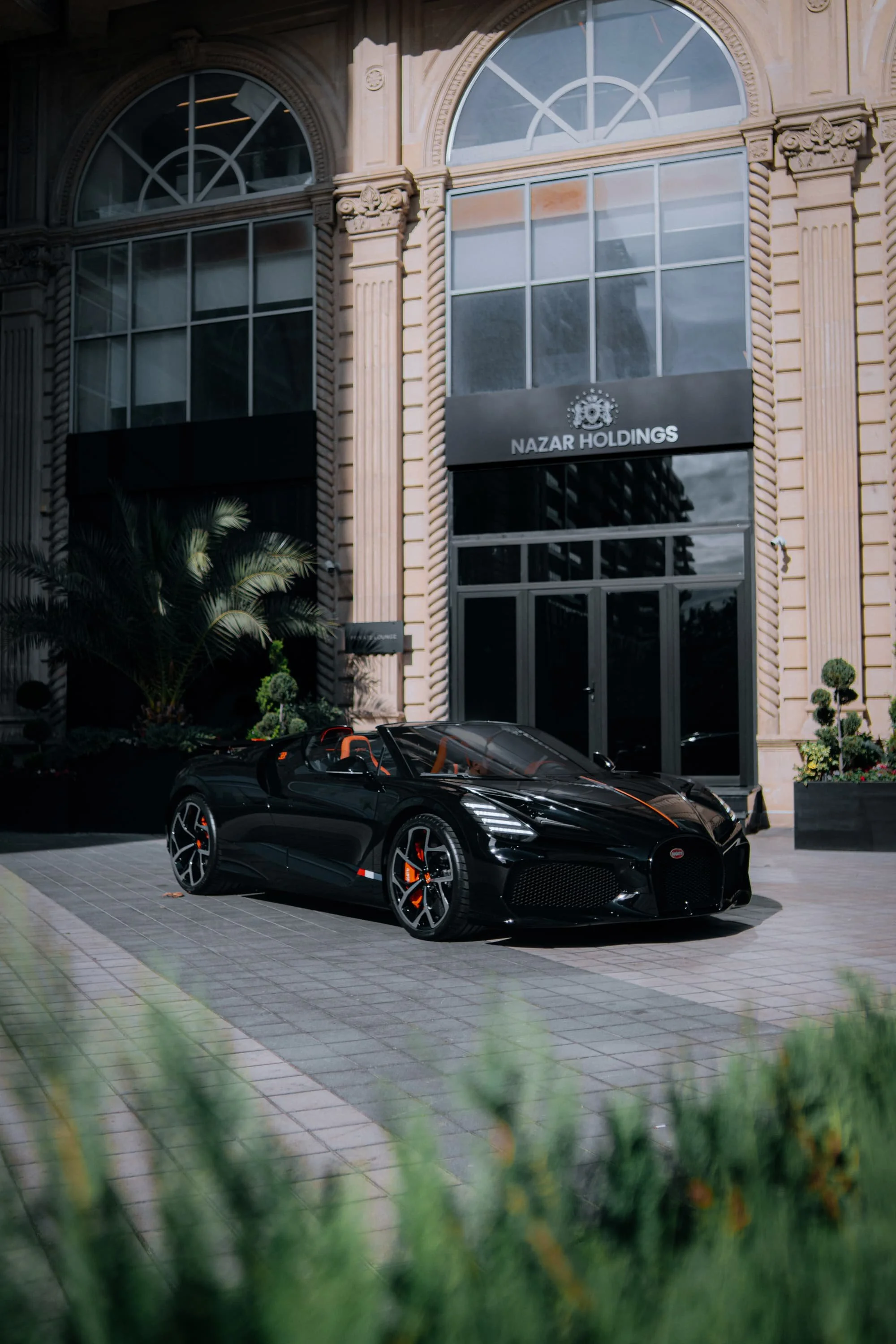 A black Bugatti Chiron parked in front of a modern building with a sign that reads 'Nazar Holdings'.