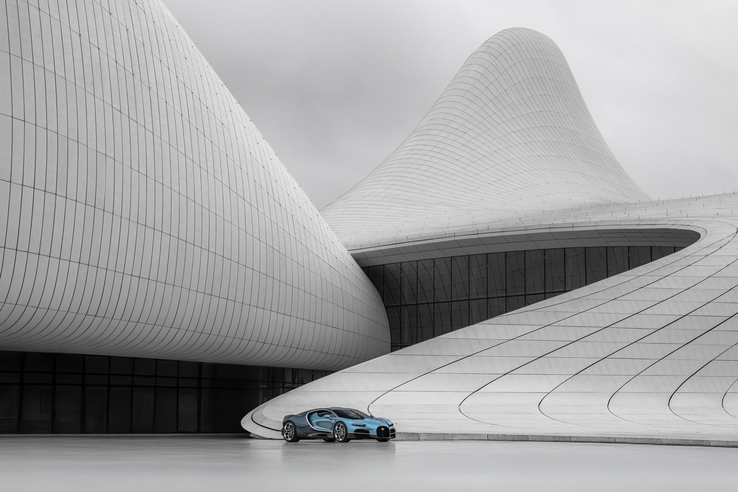 A luxury sports car parked in front of a modern, futuristic white building with curved, flowing architecture.