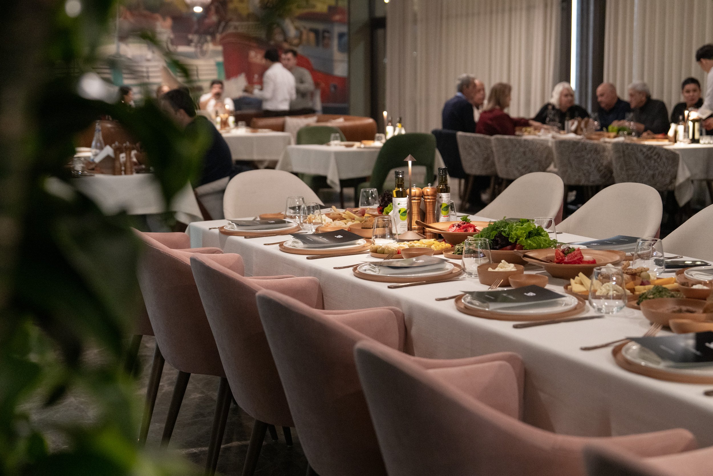 A dining table set with plates, glasses, and food in a restaurant with other diners and waitstaff in the background.