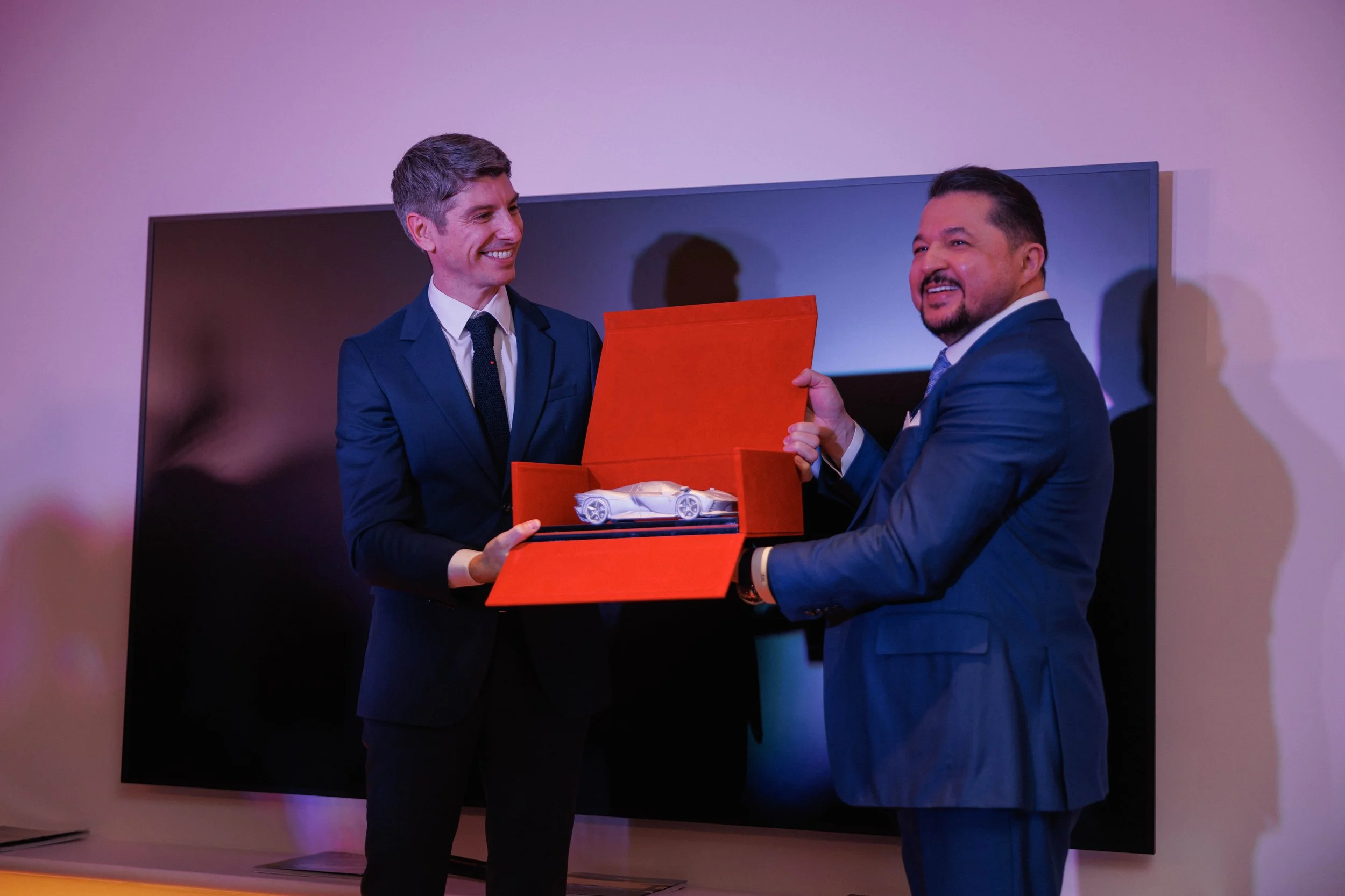 A blue sports car with its gull-wing door open, parked in front of a modern architectural building with curved white walls and large glass windows.