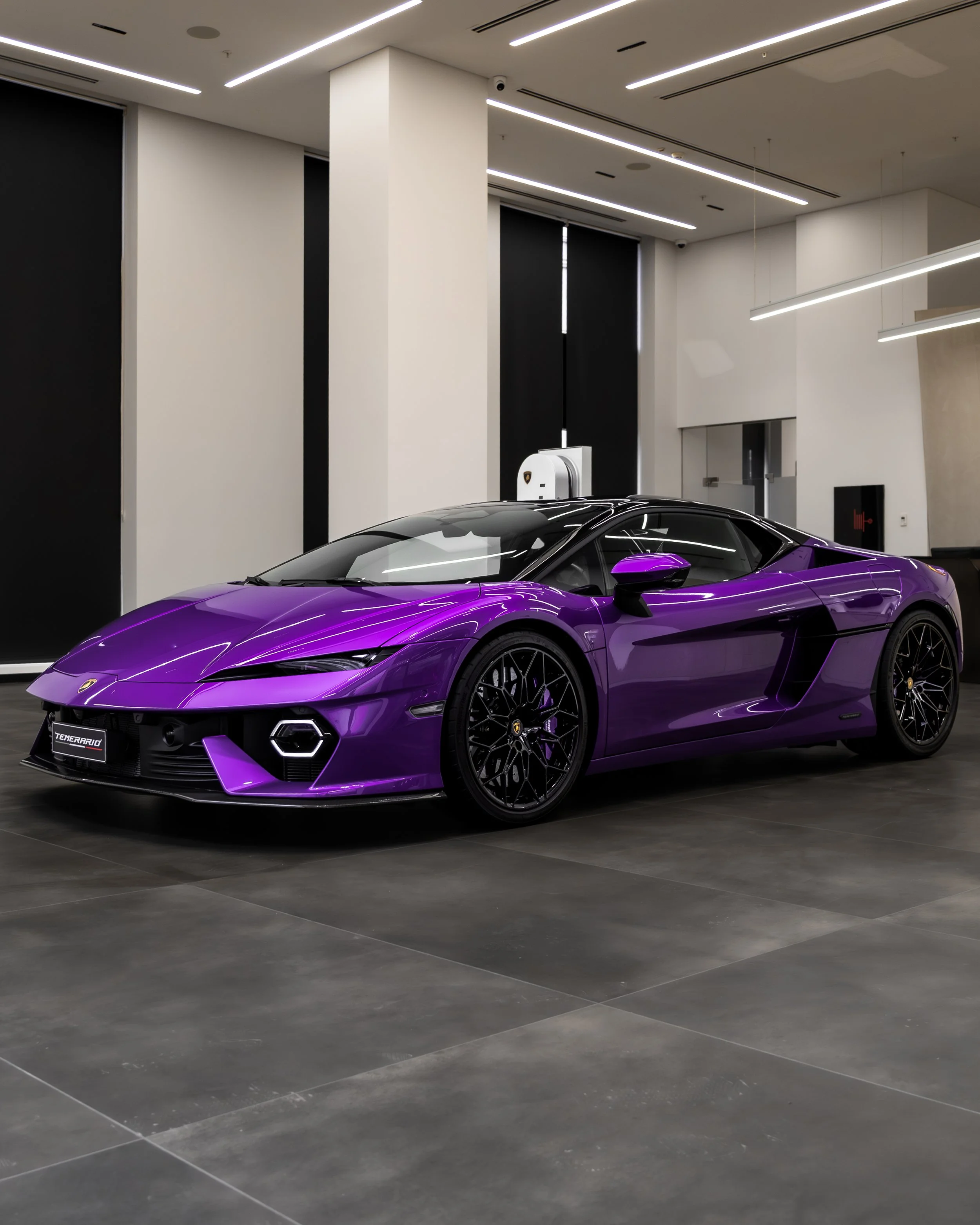 A purple luxury sports car is displayed indoors on black flooring, with modern white and black interior decor.