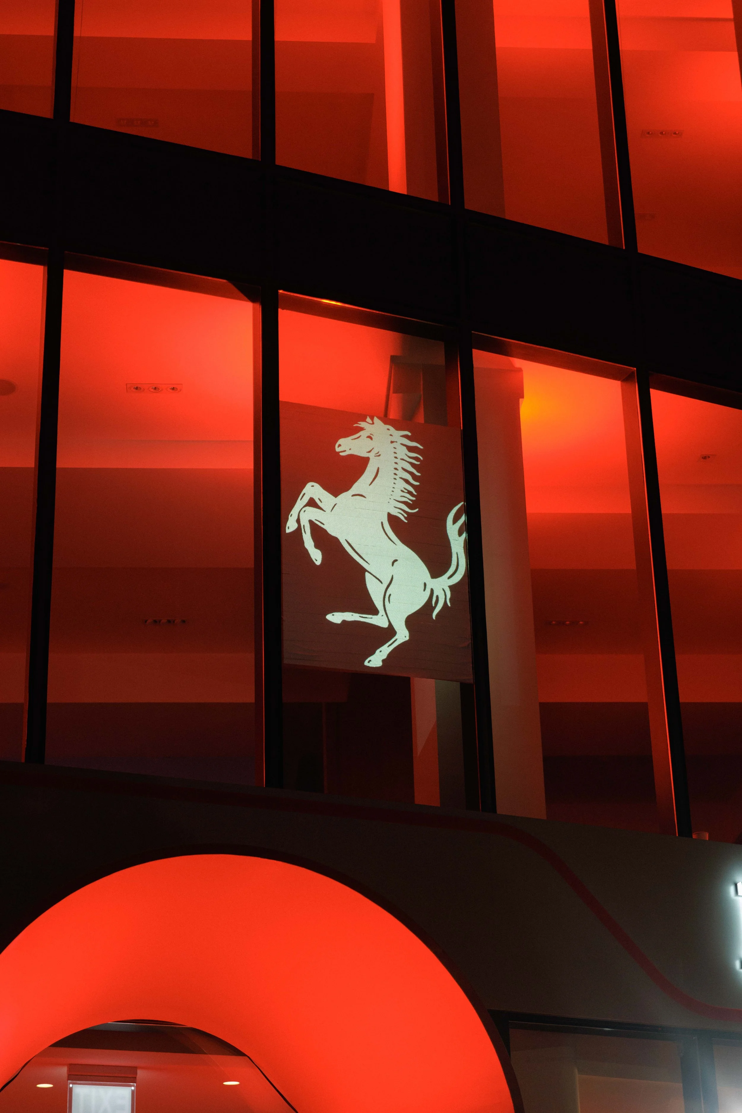 Multistory building with large illuminated Ferrari logo featuring a prancing horse, accentuated by red lighting.