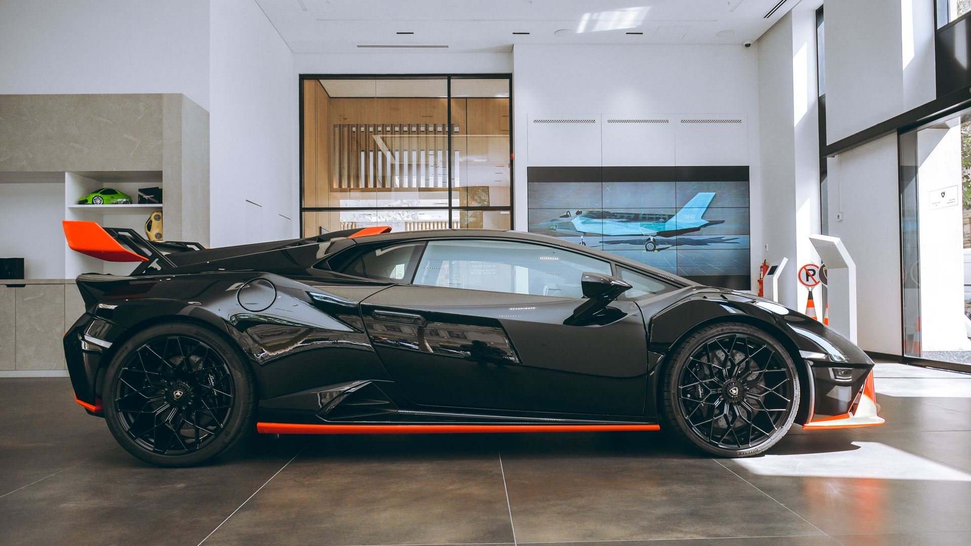 Black and red luxury sports car on display at a dealership with indoor setting and large windows showing outside.