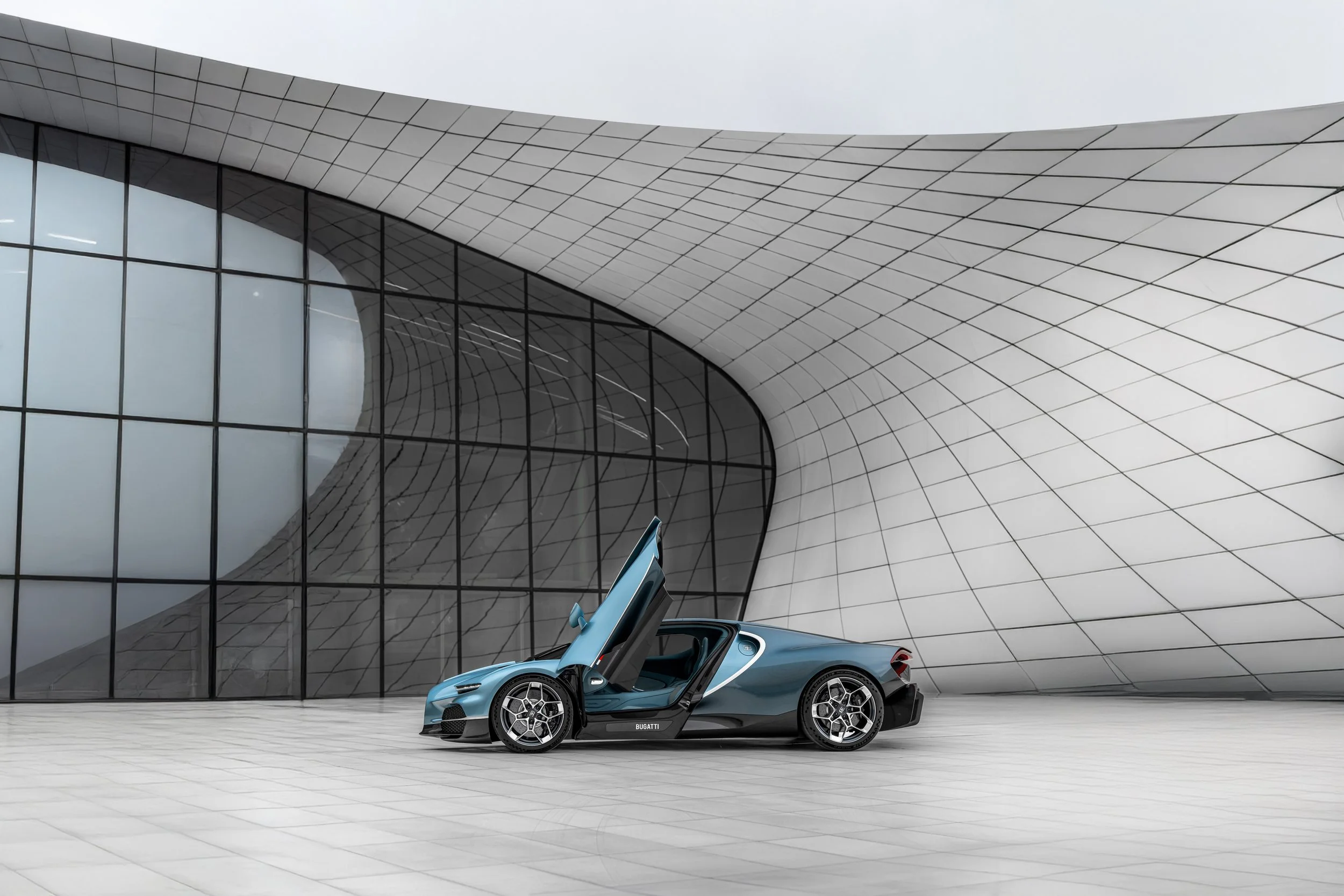 A blue sports car with its gull-wing door open, parked in front of a modern architectural building with curved white walls and large glass windows.