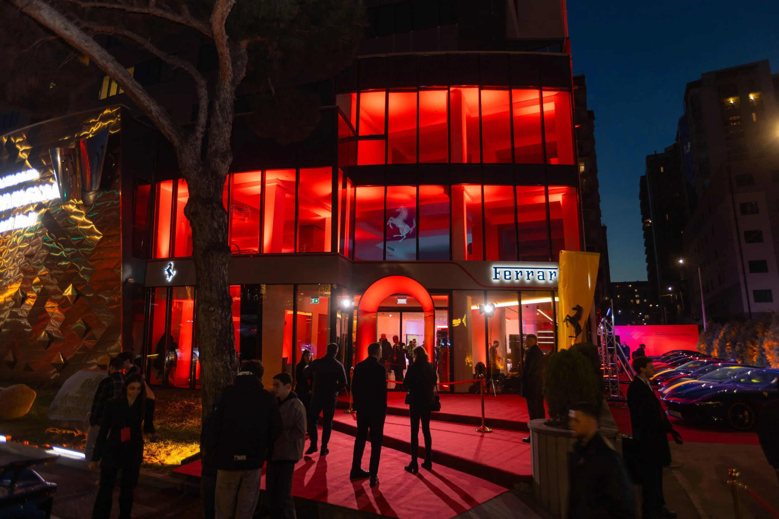 A sleek, blue Bugatti sports car parked in front of a modern architectural building with large glass windows and curved, white panels.