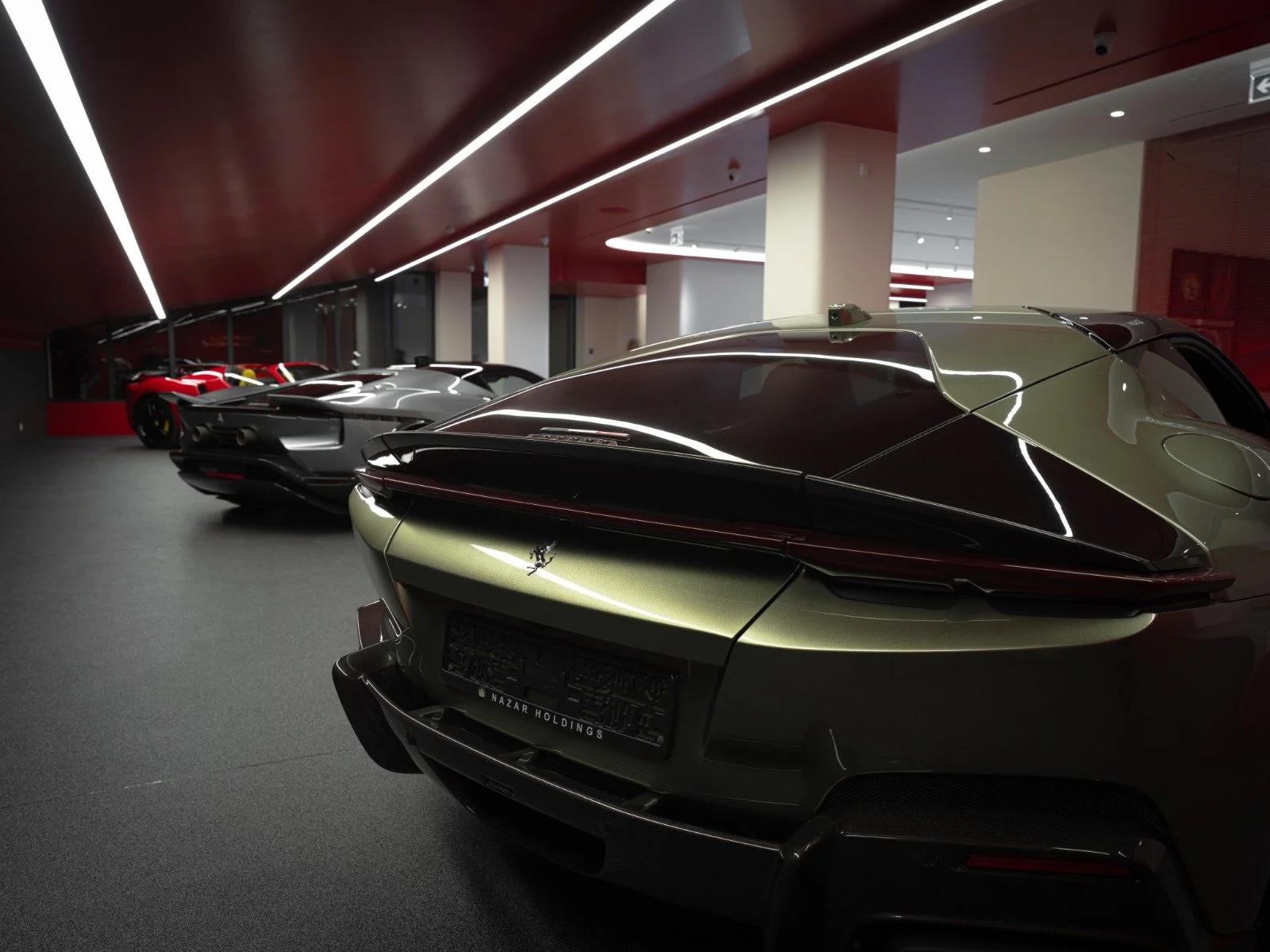 Multiple luxury sports cars parked inside a showroom, with the closest car being a green Ferrari.