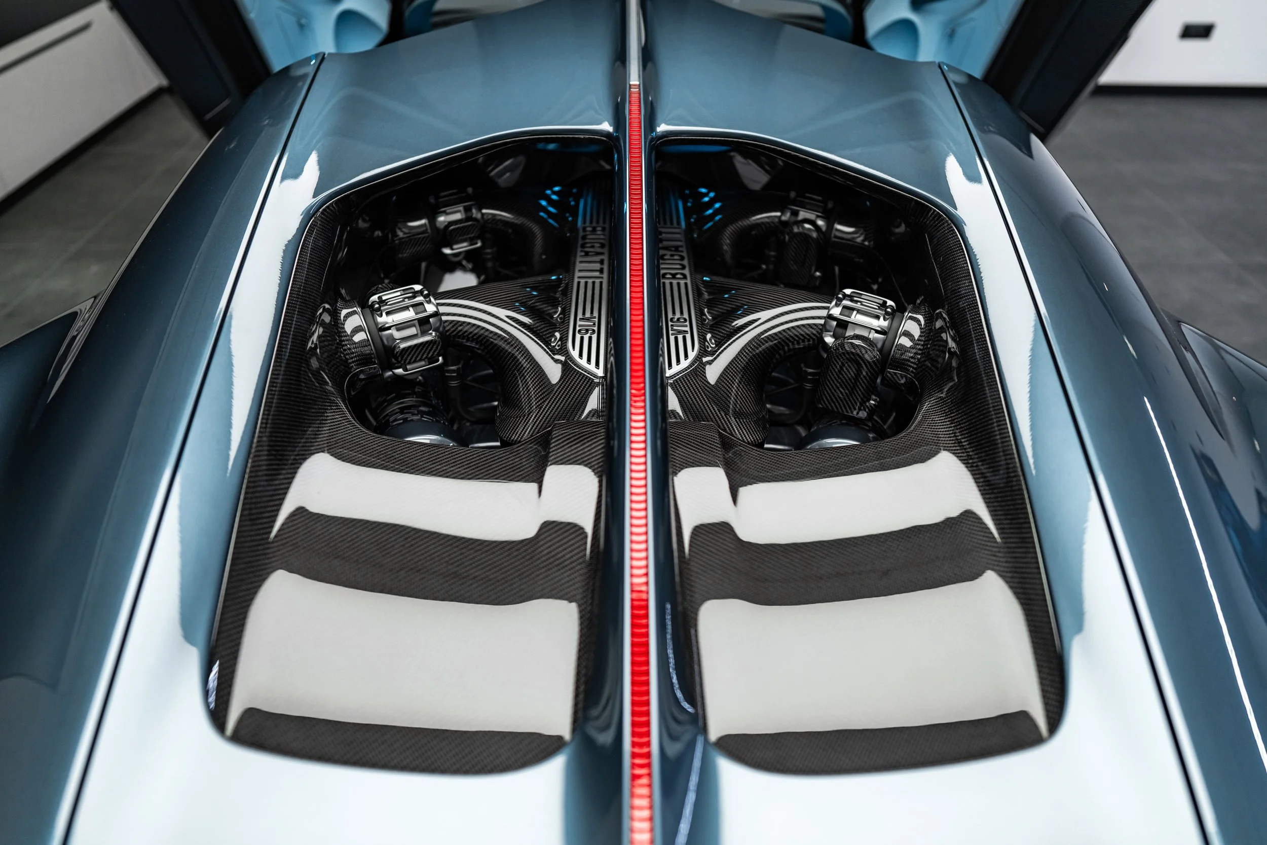 Top view of a blue sports car with its engine visible through rear glass, featuring carbon fiber components and the Bugatti logo.