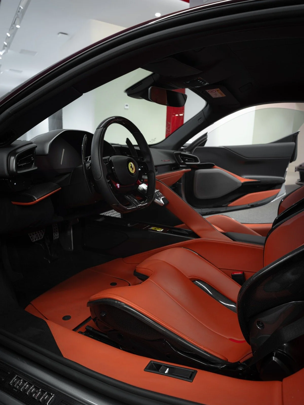 View of the interior of a luxury sports car, Ferrari, with orange leather seats, black dashboard, and steering wheel.