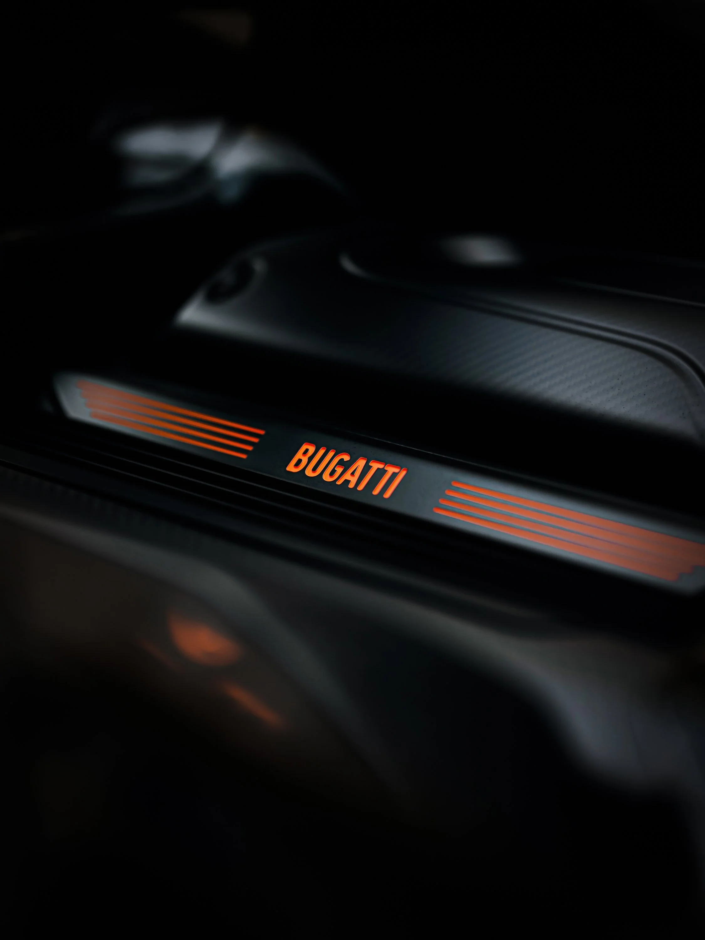 Close-up of a Bugatti logo illuminated in orange on a dark car interior.