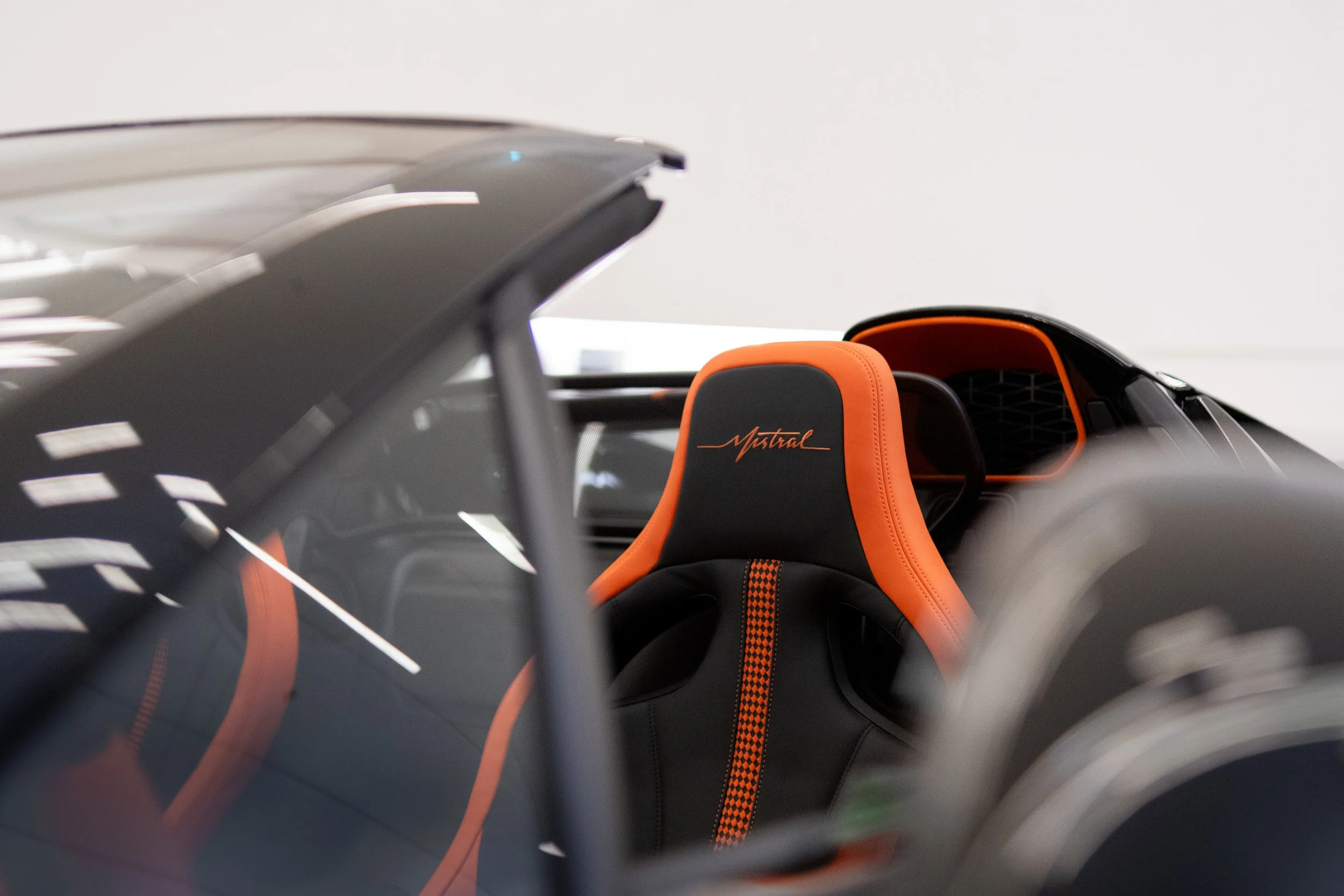 Close-up of a race car's interior showing a racing seat with orange and black color scheme and the word 'Astral' embroidered on the headrest.