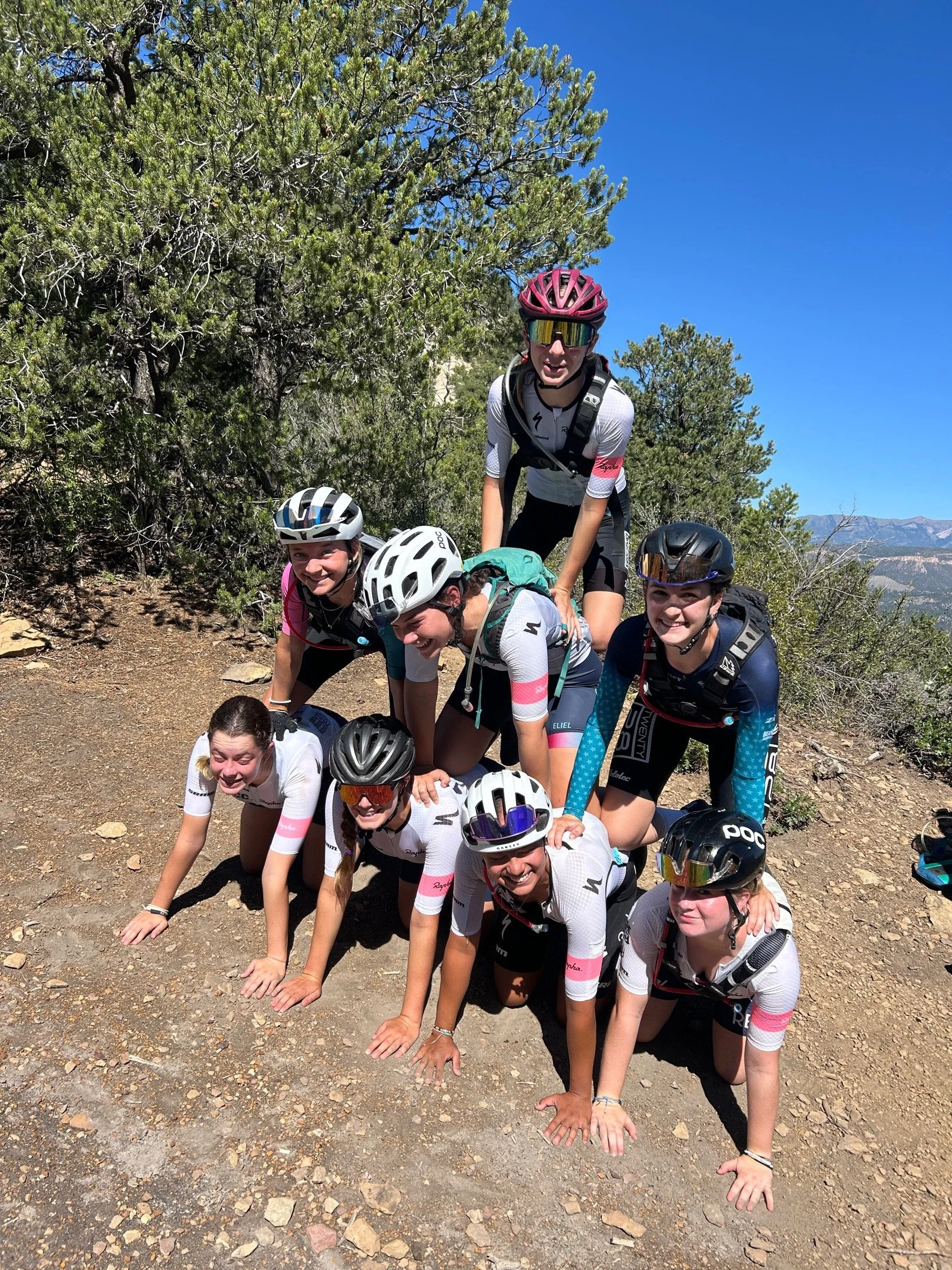 Beyond Racing riders forming a playful pyramid on a mountain trail during a break.