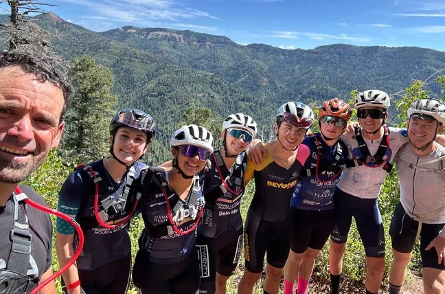 A coach and group of BEYOND Racing riders posing together with arms around each other on a mountain overlook in Durango, Colorado.