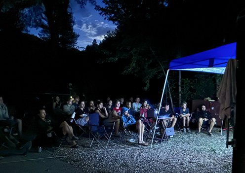 BEYOND Racing riders and coaches sitting together at a nighttime campsite gathering under string lights.