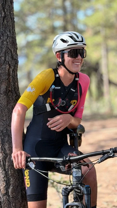 A Beyond Racing rider resting against a tree next to their mountain bike on a wooded trail.