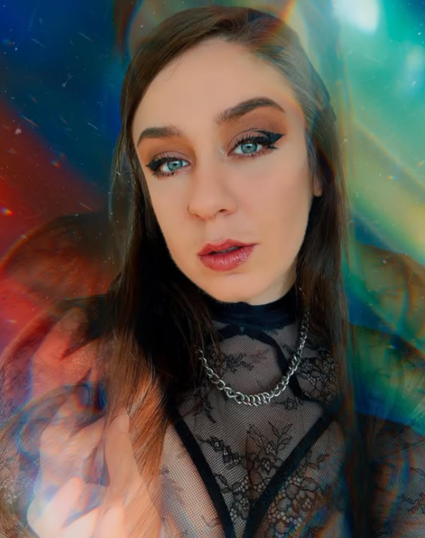 A young woman with blue eyes and brown hair wearing a black lace top and silver chain necklace, posing in front of a colorful, abstract background.