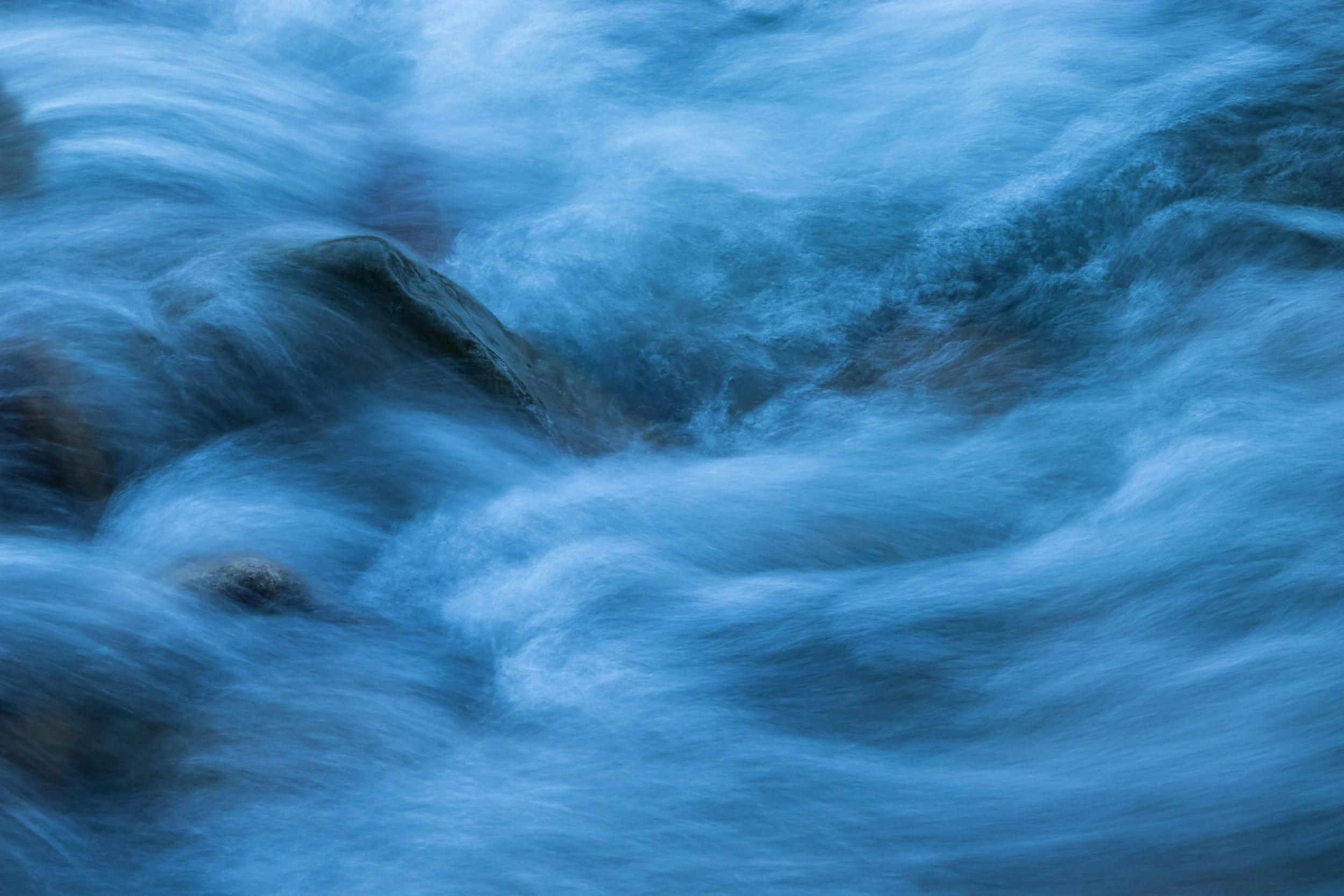 Photo of flowing water in a moody blue color tumbling against a rock