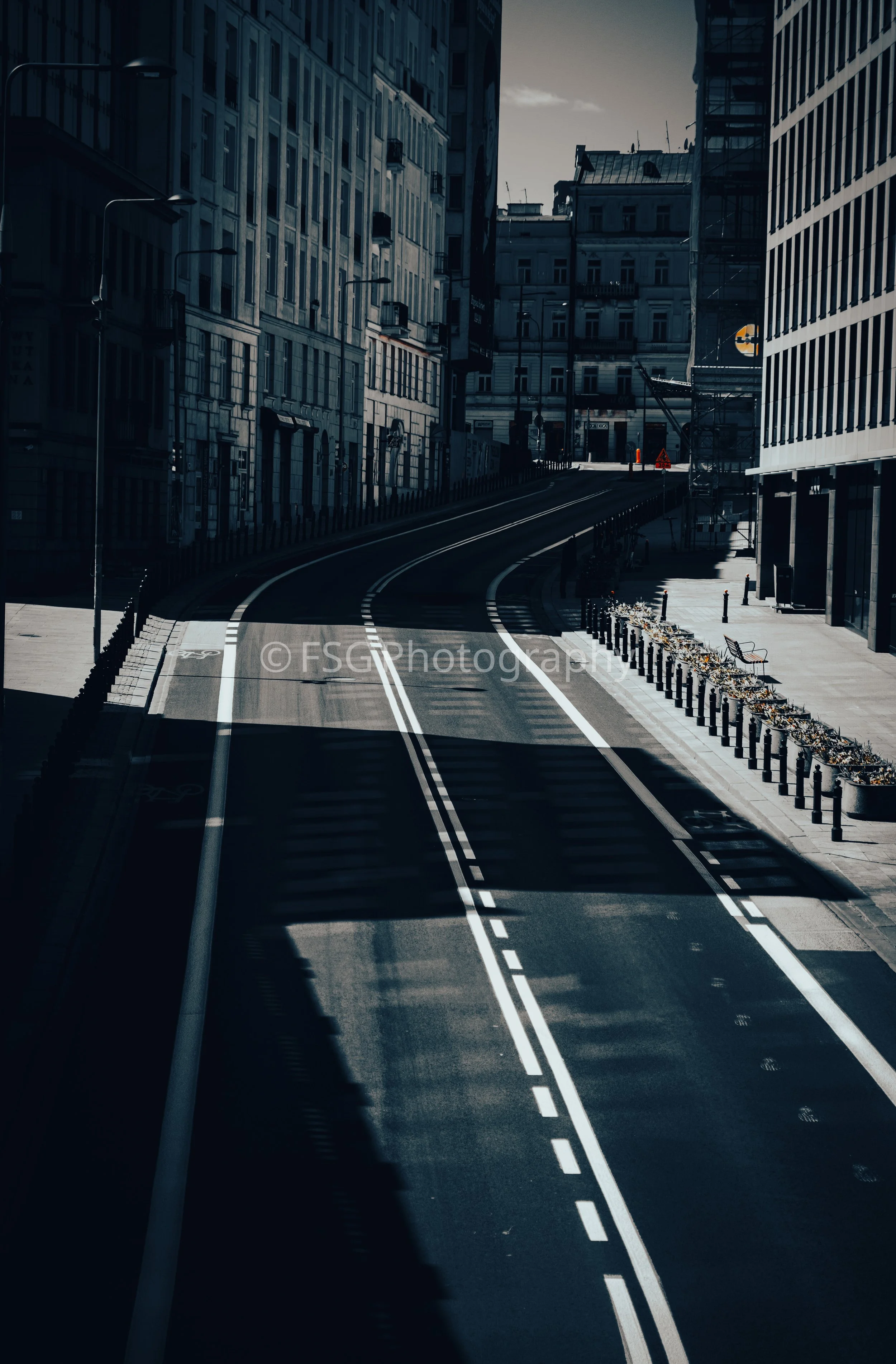 Shadowed Transit

A striking urban landscape highlighting the dramatic play of light and shadow across a curved city street. A minimalist look at urban life, where empty roads and sharp shadows tell a story of a city at rest.
