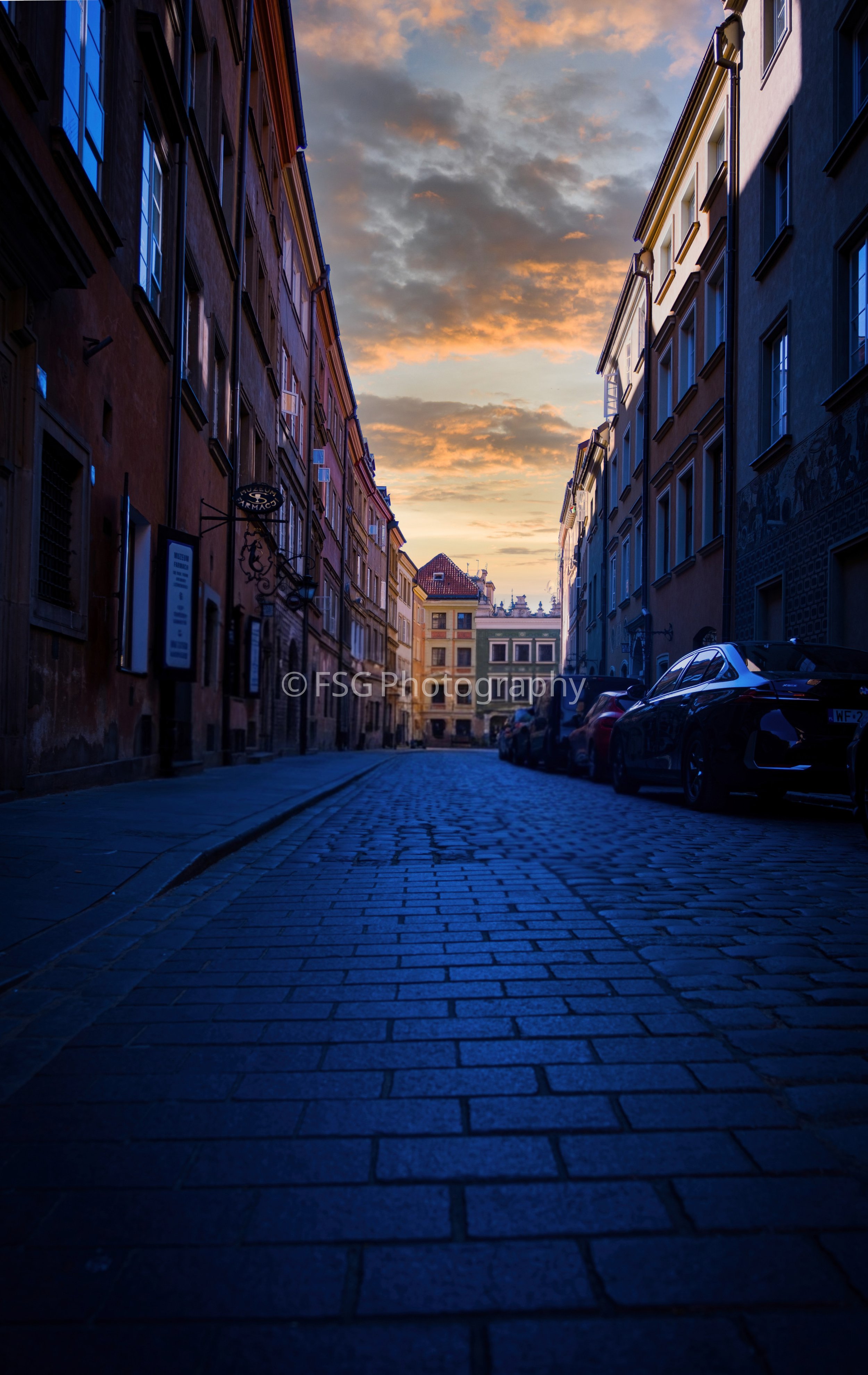 Chasing the Amber Hour

Captured along the cobblestones of Warsaw's historic Old Town, this piece explores the striking contrast between the cool shadow tones of the narrow street and the warm, fiery hues of a Polish sunset. The composition uses natu
