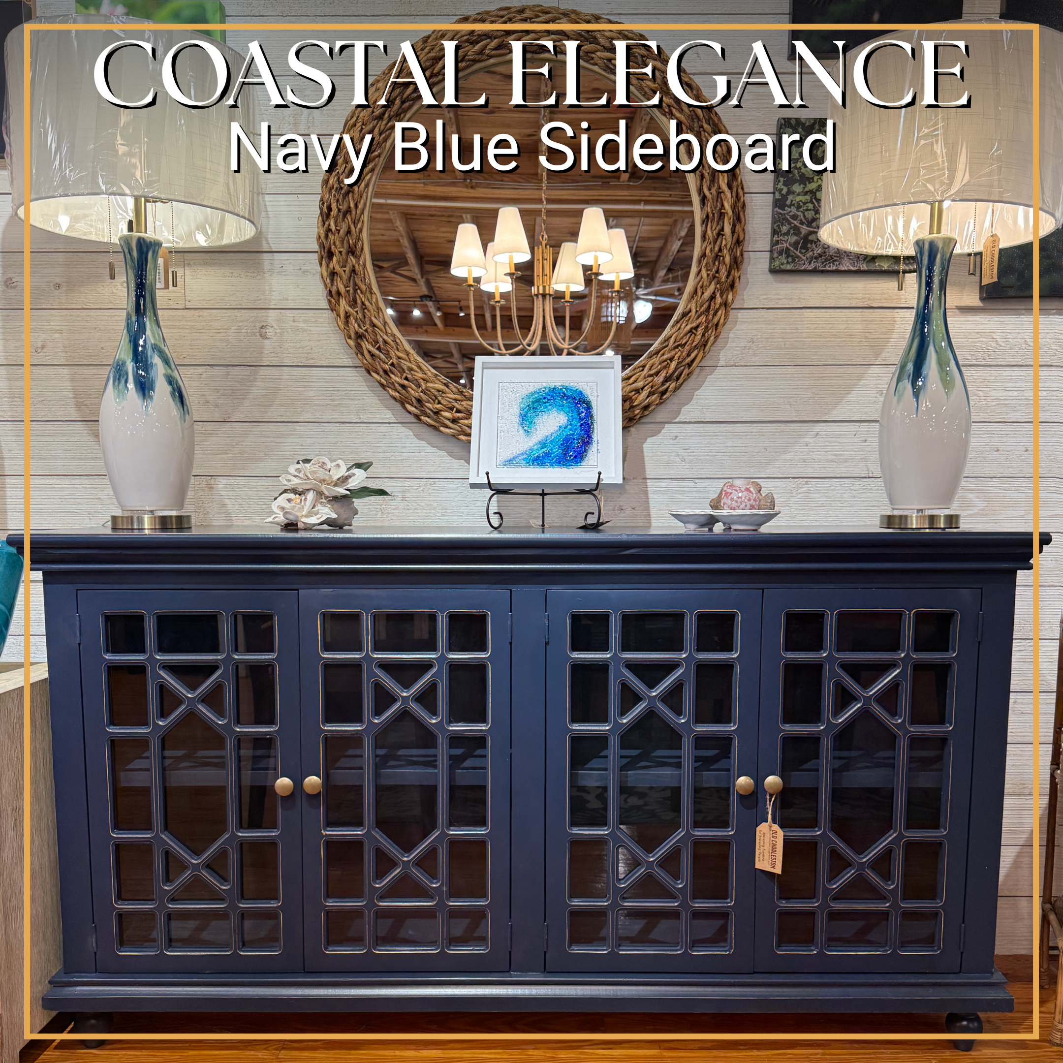A dark blue sideboard with glass-paneled doors, two table lamps with white shades and blue and green vases on top, a round woven mirror, and decorative items including a framed artwork of a blue number 2.