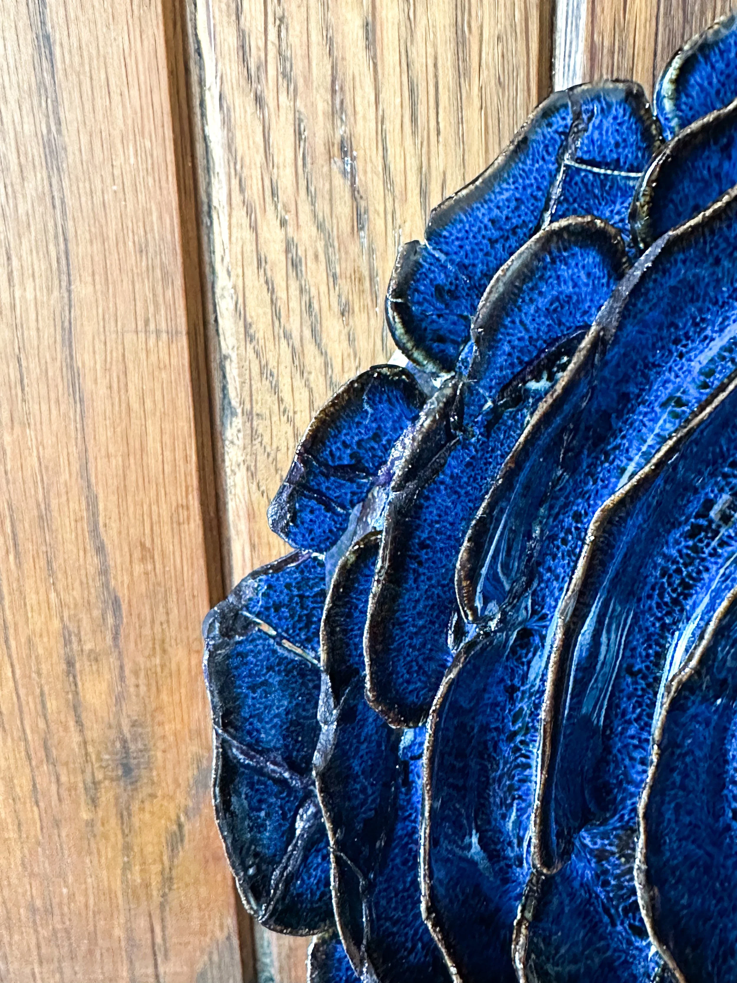 Close-up of a blue sculptural flower with broken pieces glued together against a wooden background