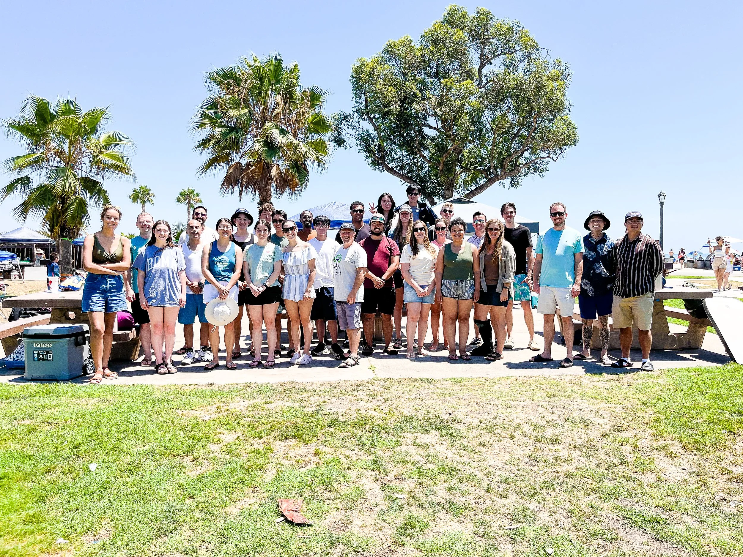 A large group of Oceanside URC's young adults standing outdoors in front of trees and blue sky, posing for a photo on a sunny day.