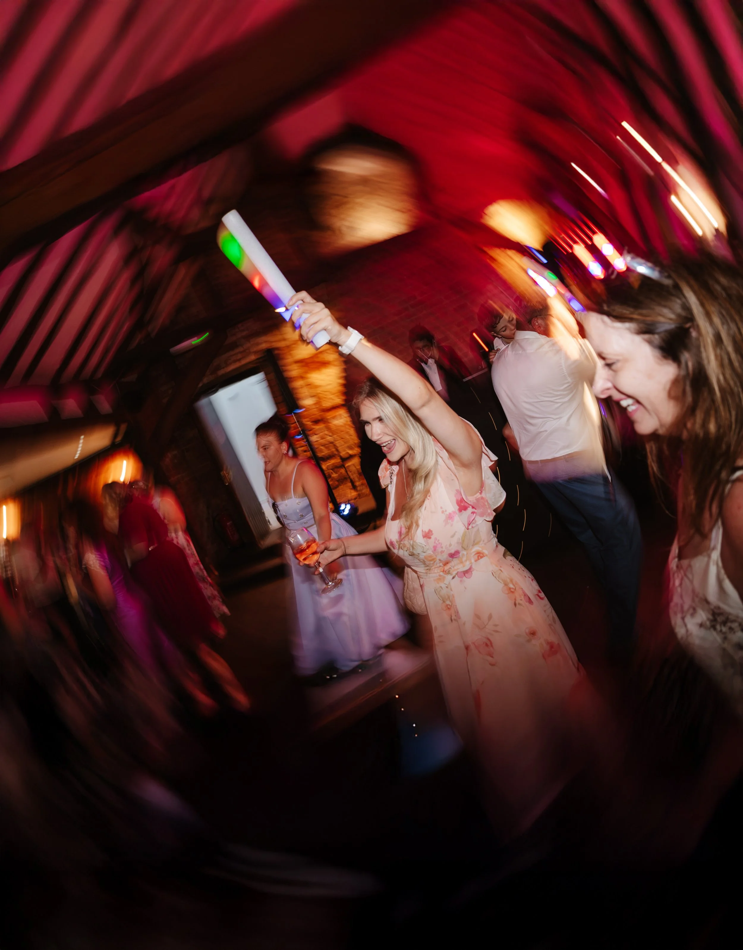 People dancing and having fun at a party or celebration in a dimly lit venue with vibrant red and pink lighting.