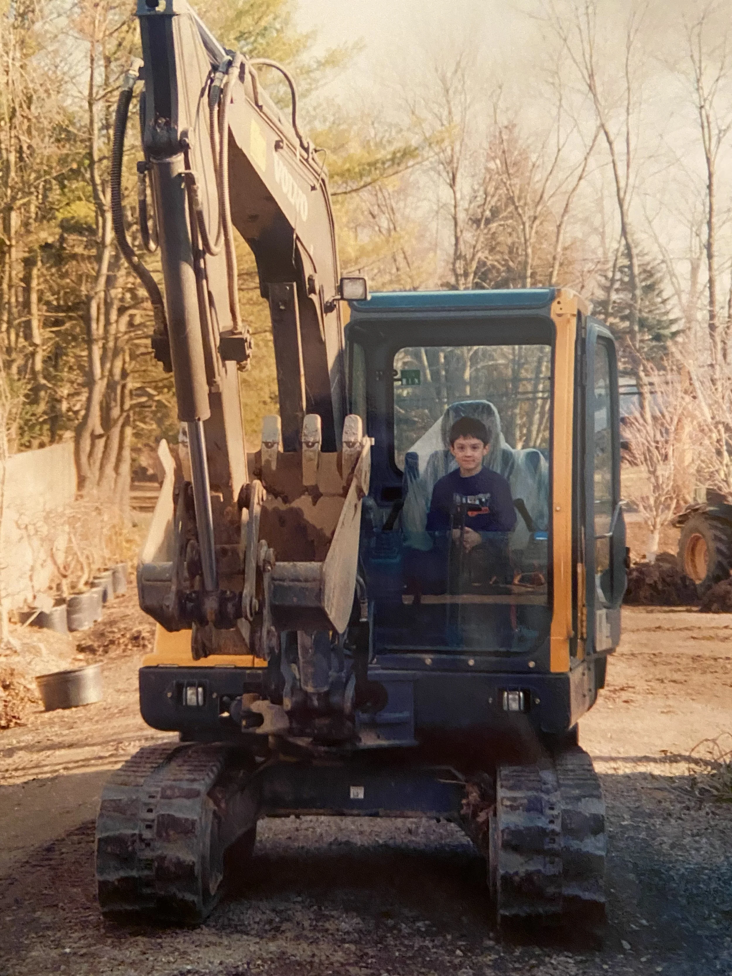 A young boy sitting inside a yellow and black construction excavator at a construction site during daytime.