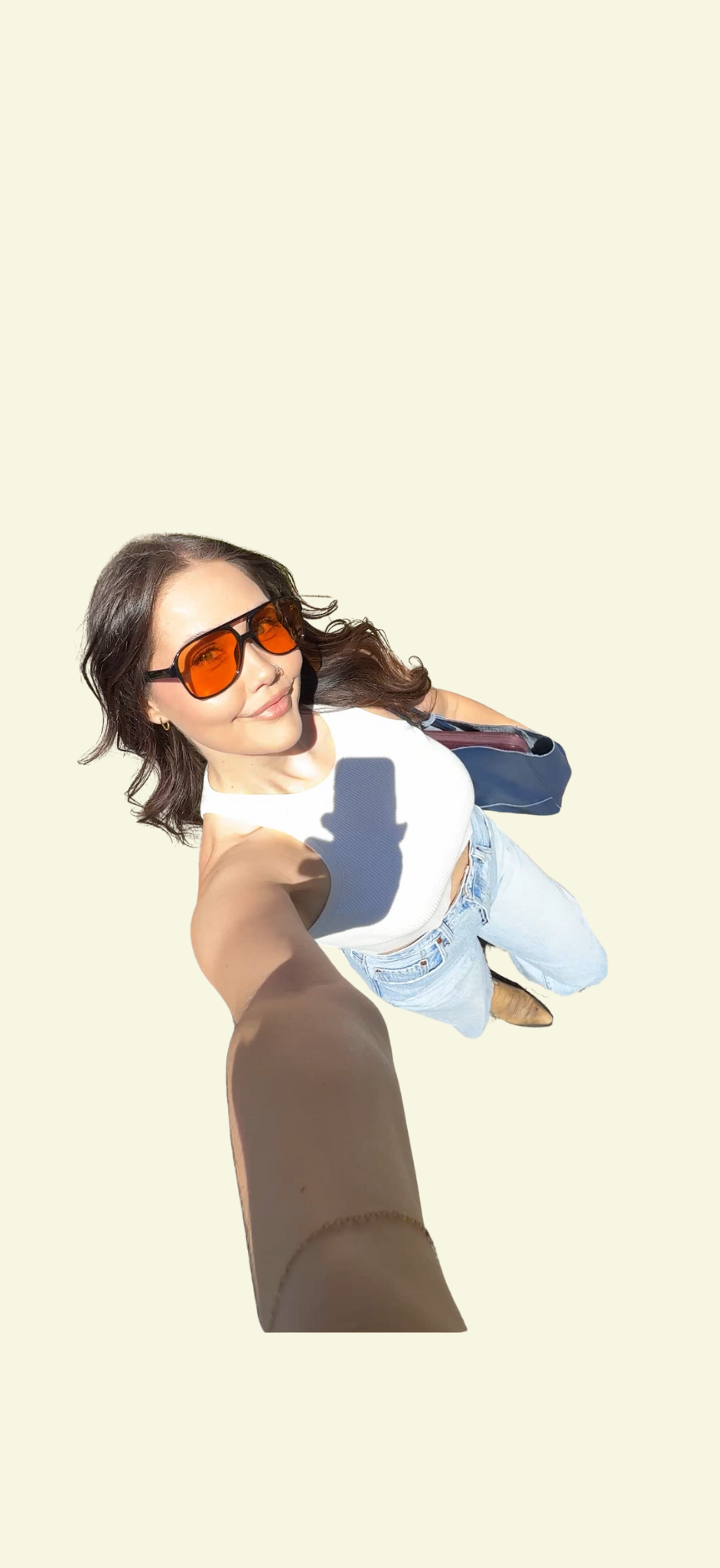 A young woman influencer taking a selfie from a high angle, wearing sunglasses, a white sleeveless top, jeans, and brown boots, with her arm extended to hold the camera against a plain, light background - instagram, tiktok, social media vibes.