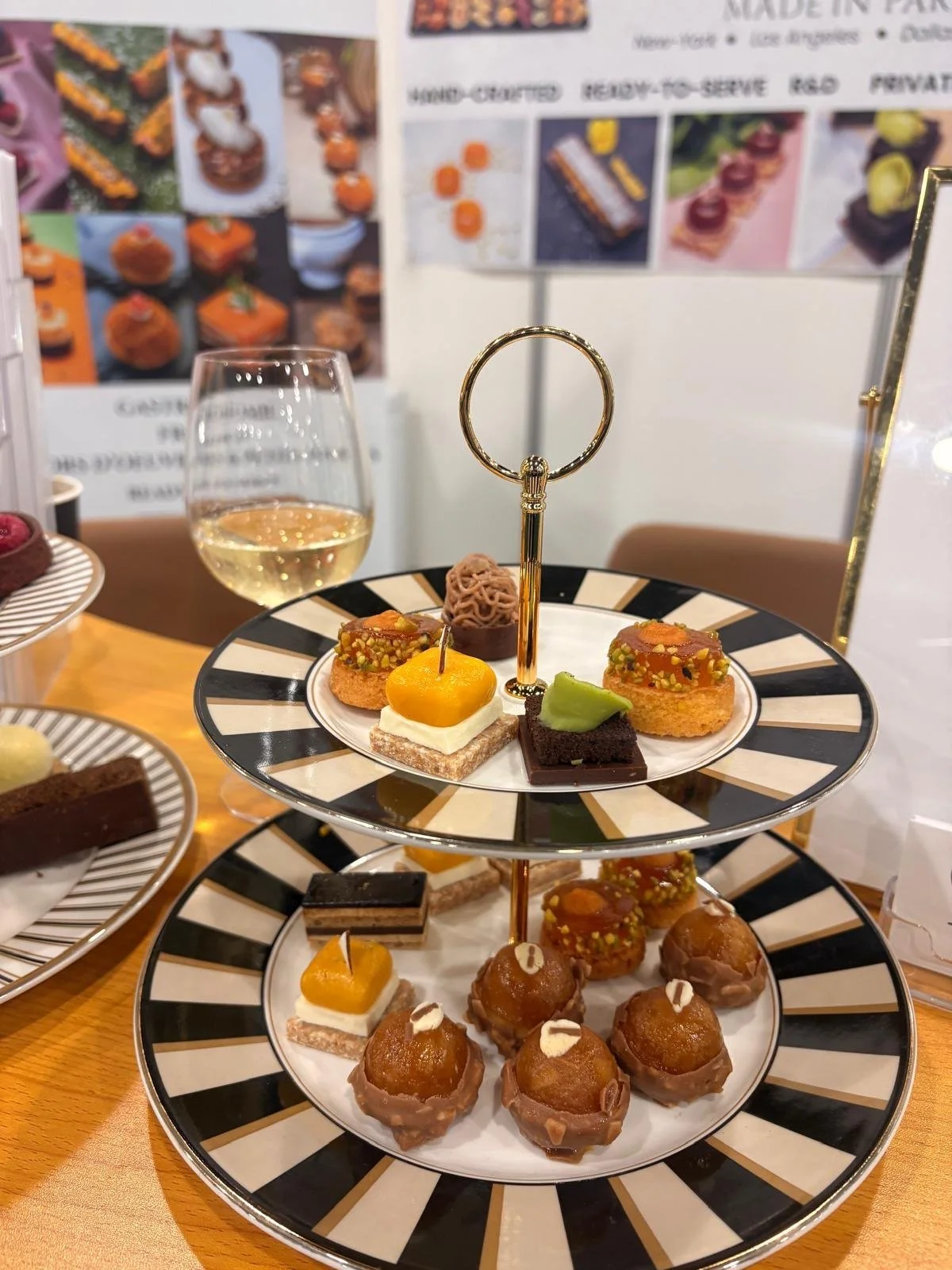 Tiered stand of French mini desserts for premium cabin service, including mango petits fours, caramelized rounds with pistachio, a chestnut dessert and a mini opera