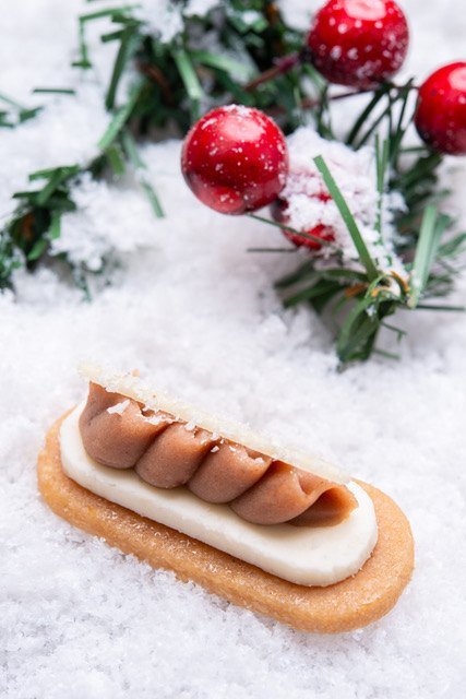 Caramel petit four with piped caramel cream over a white layer on a biscuit base, topped with a thin sugar sheet, in a snowy holiday setting