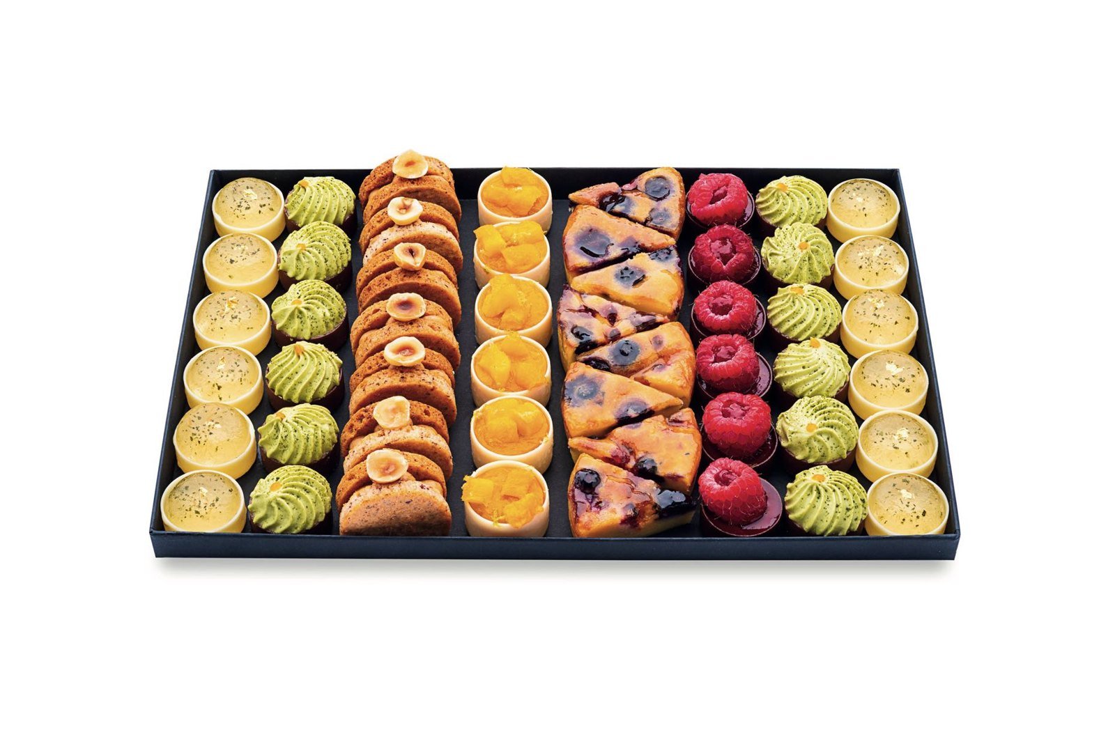 Tray of French petits fours in rows of colorful mini tartlets with lemon, pistachio and red fruit toppings on a black serving tray