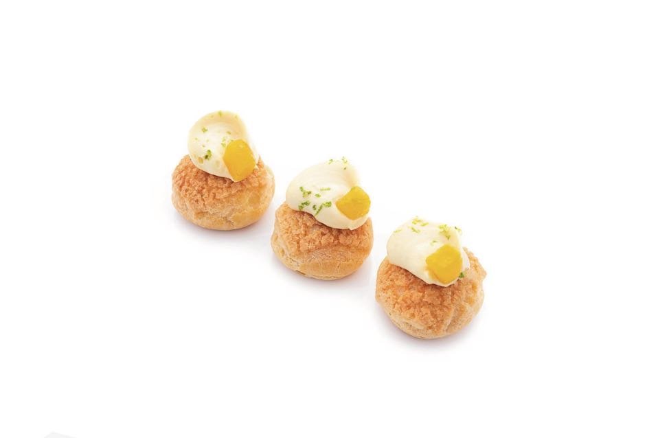 Three mango passionfruit mini puffs, golden crackle choux pastries topped with cream and a fresh mango cube