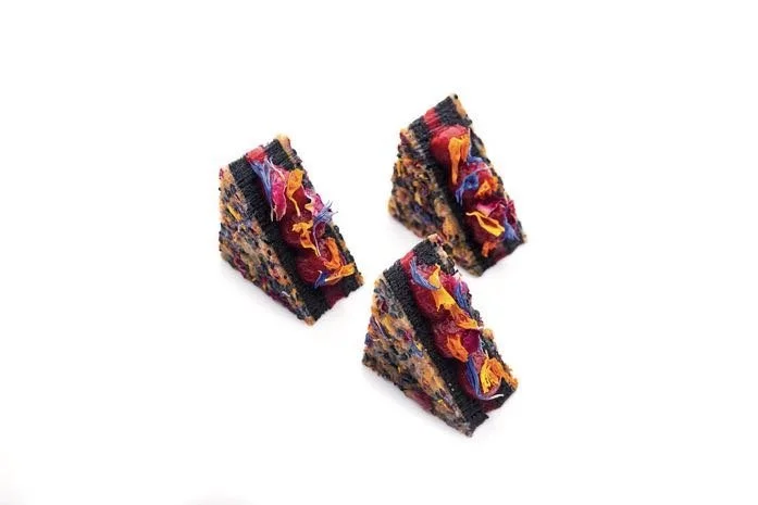 Three triangular sesame and raspberry petits fours with a dark black sesame cake and bright dried flower finish
