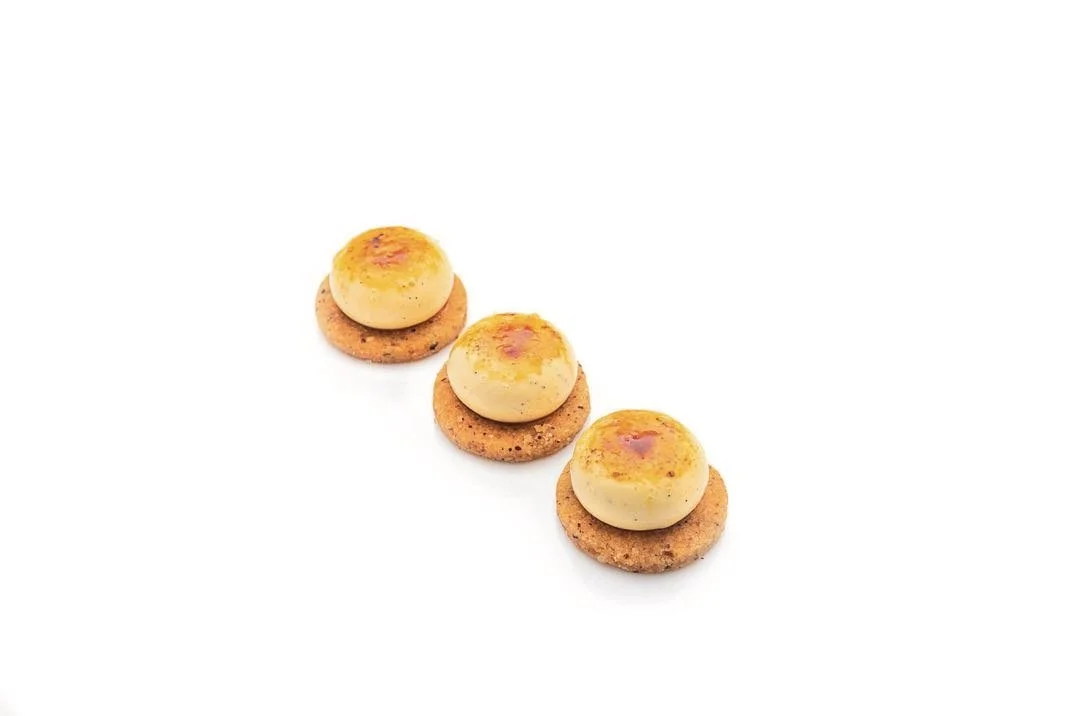 Three mini crème brûlée petits fours with a torched golden top on a hazelnut biscuit base