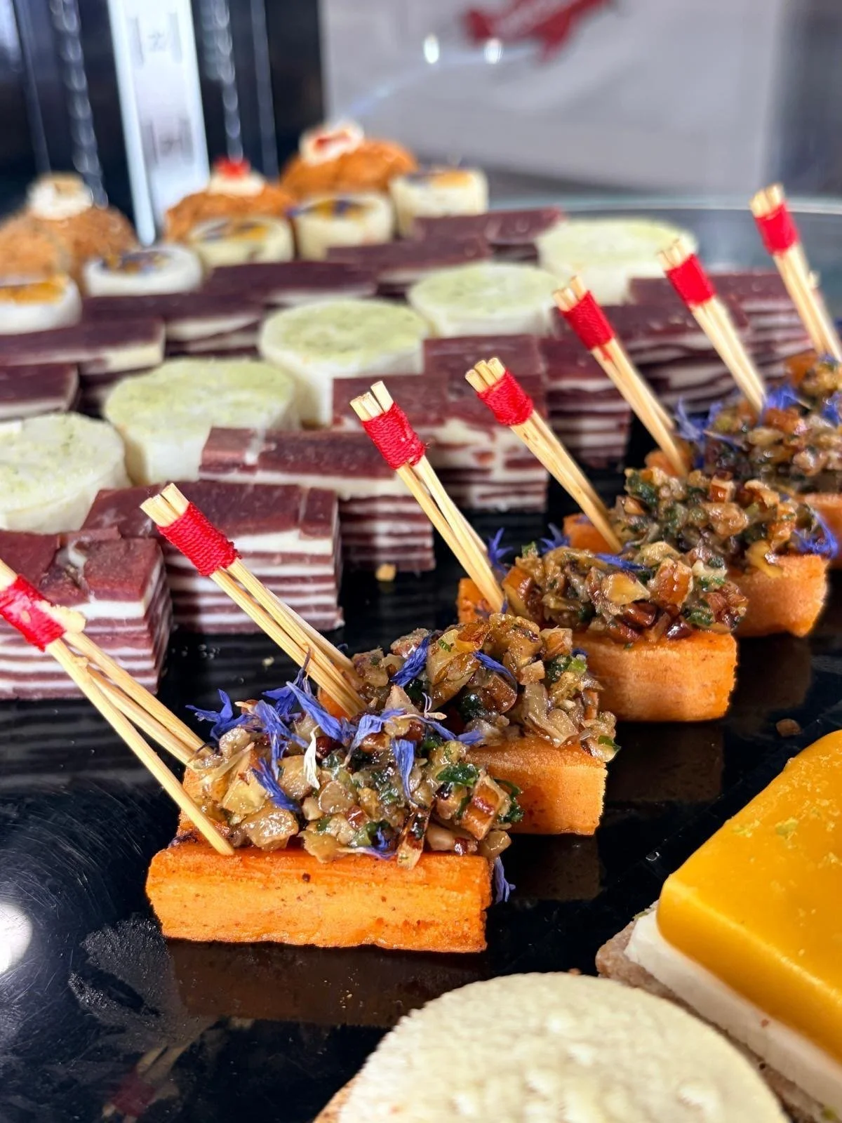 Close up of savory petits fours salés, sweet potato canapés topped with a nut and herb mix and blue cornflower petals, beside layered savory bites