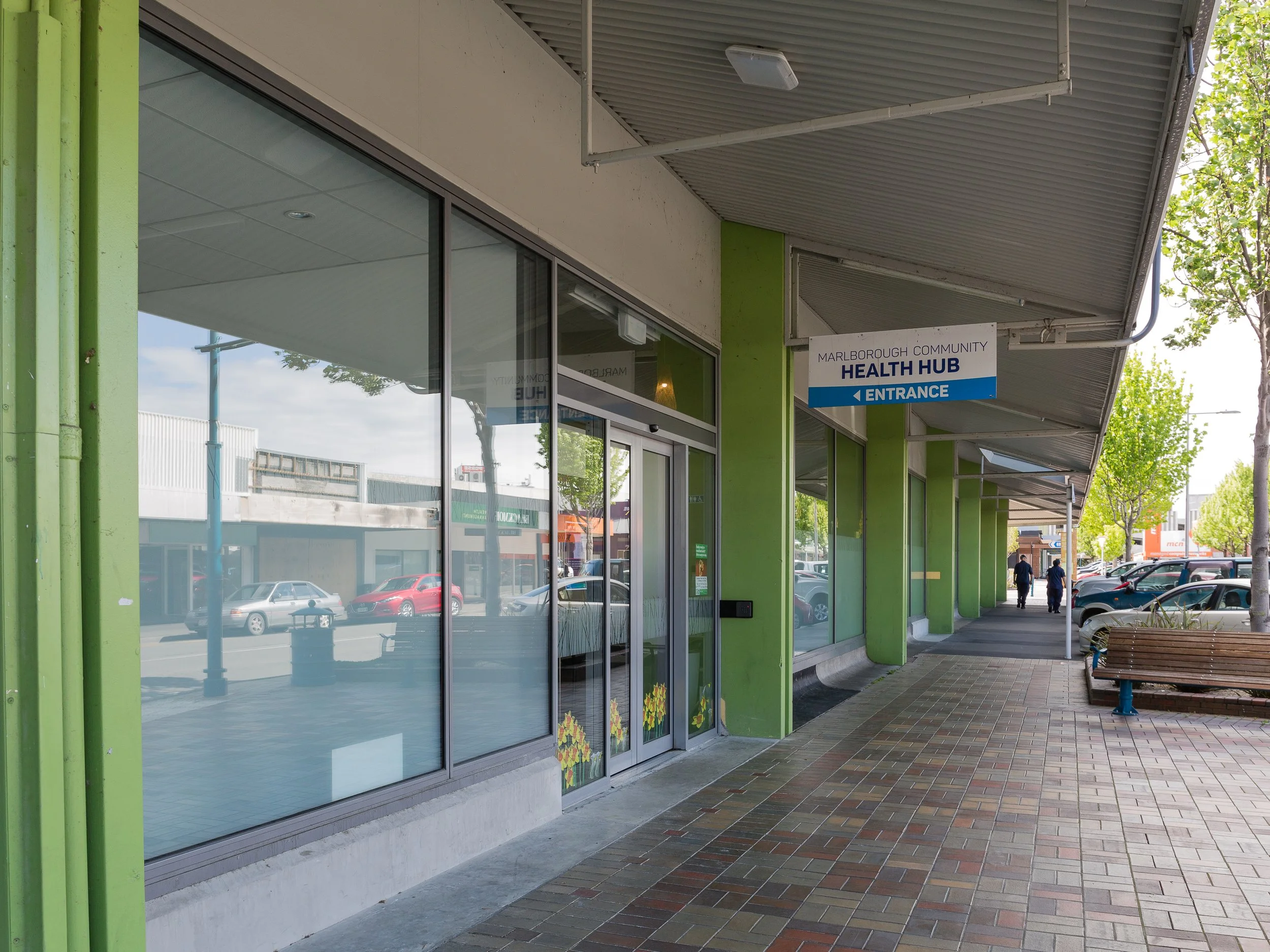 Exterior view of a healthcare facility named CIVIC FAMILY HEALTH CARE with glass doors, parked cars, and scooters in front.