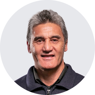 A middle-aged man with gray hair and a friendly expression, wearing a dark zip-up jacket over a collared shirt, against a light background with a black curve in the top left corner.