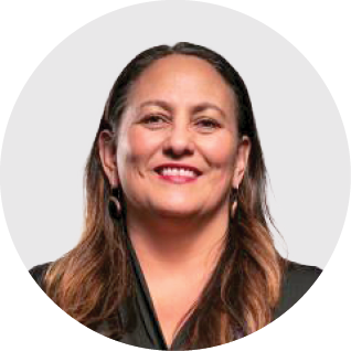 A woman with shoulder-length hair smiling, wearing a black top and earrings, against a plain background.