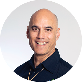 A smiling middle-aged man with a bald head, wearing a dark collared shirt, posing against a plain background.
