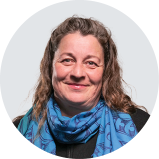 A woman with curly hair wearing a black top and a blue patterned scarf, smiling at the camera.