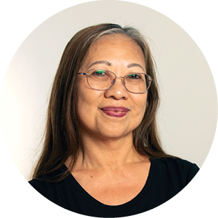 A woman with long brown hair, glasses, and a black top, smiling against a light background.