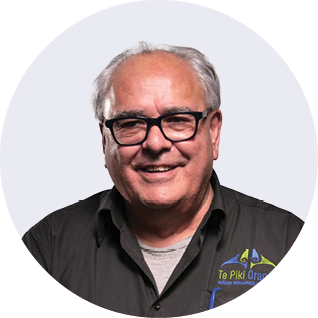 A man wearing glasses and a black vest smiling against a gray background.