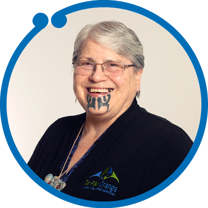 A smiling older woman with short gray hair wearing glasses and a black jacket with a logo, and a face tattoo.