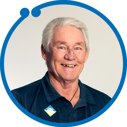 Smiling elderly man with gray hair wearing a navy blue polo shirt against a neutral background.