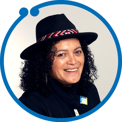 Woman with curly black hair wearing a black hat with a red, white, and black patterned band, and a black jacket, smiling at the camera.