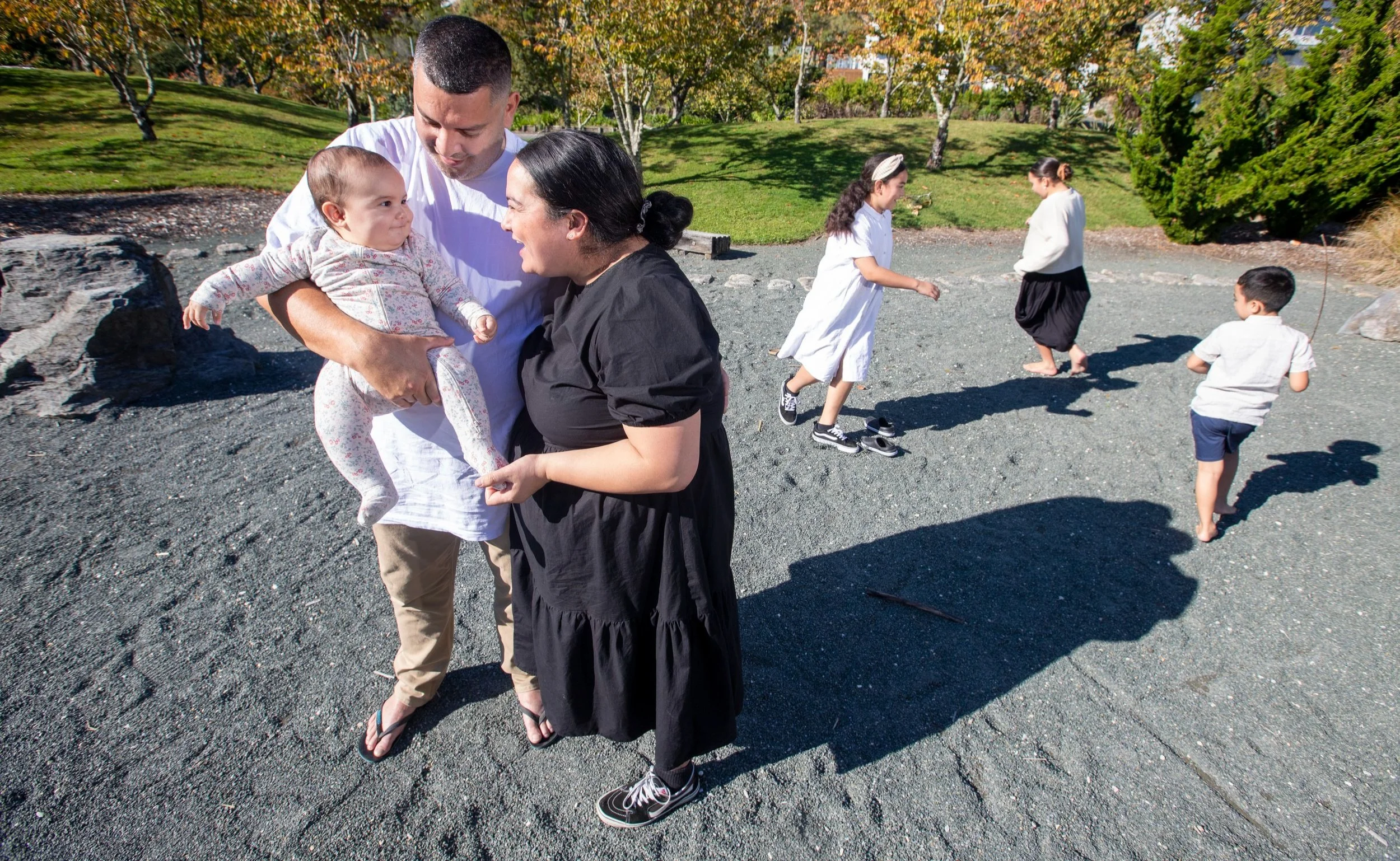 A family with young children enjoying time at the park on sunny day, with everyone playing and interacting.